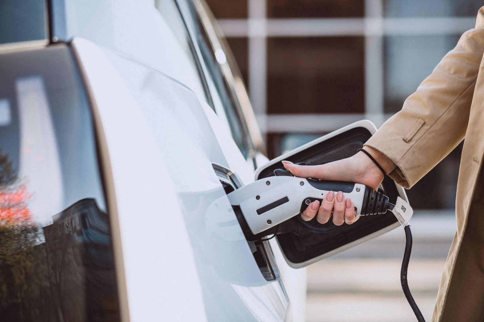 Une femme insère une prise de recharge dans une voiture électrique blanche.