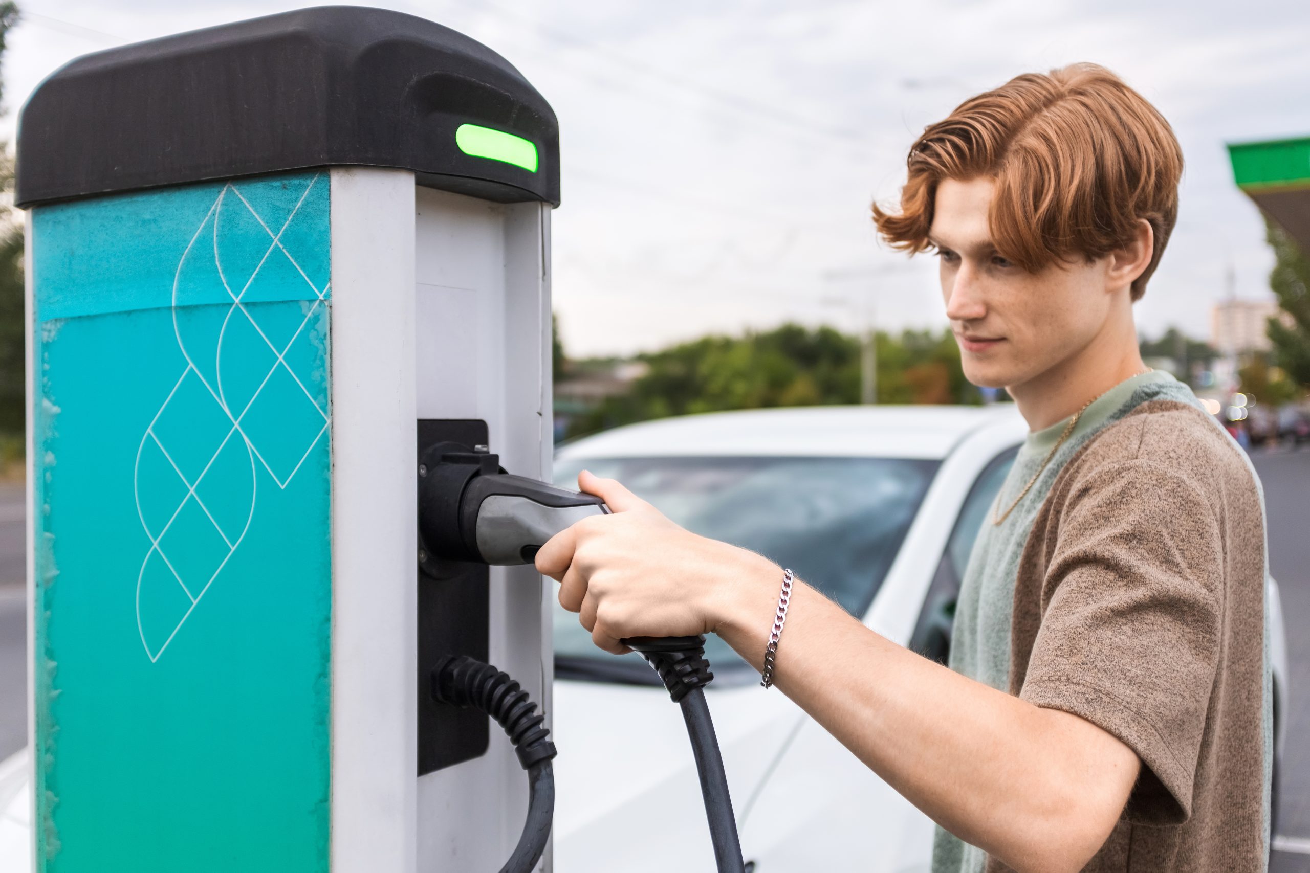 Un jeune homme branche une voiture électrique à une borne de recharge en plein air.