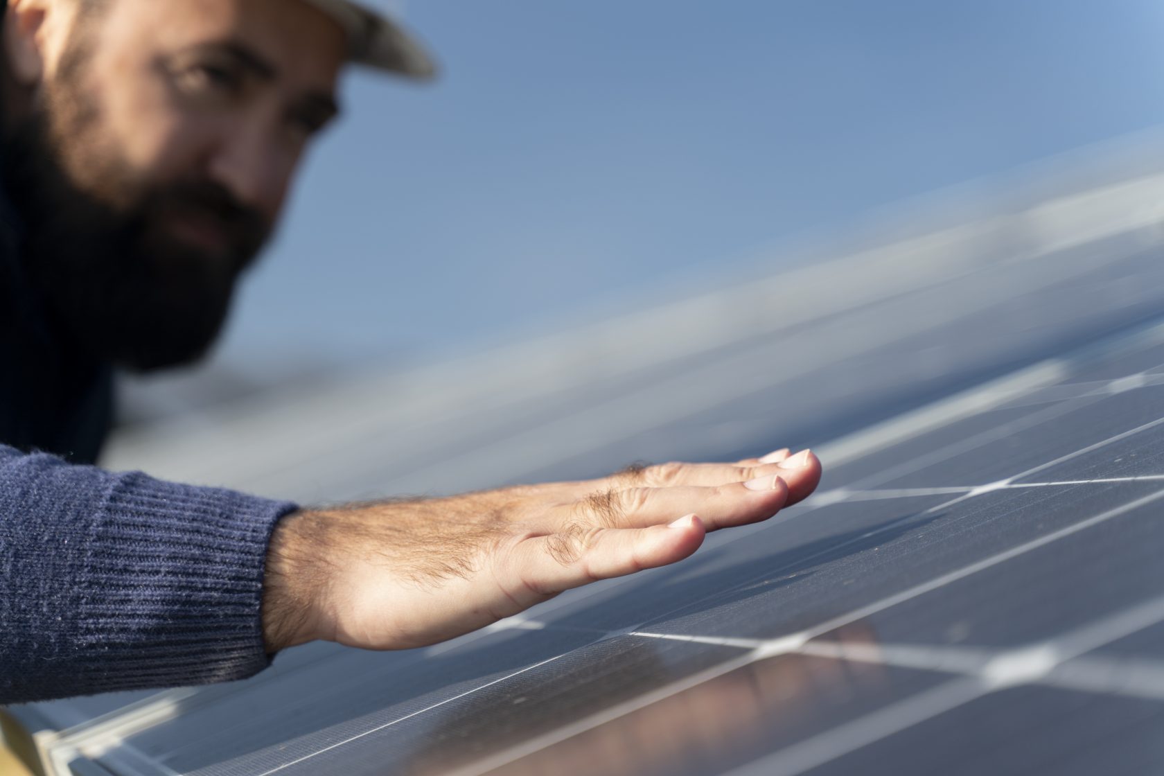 Un technicien effleure la surface d’un panneau photovoltaïque pour en vérifier l’état ou la température.