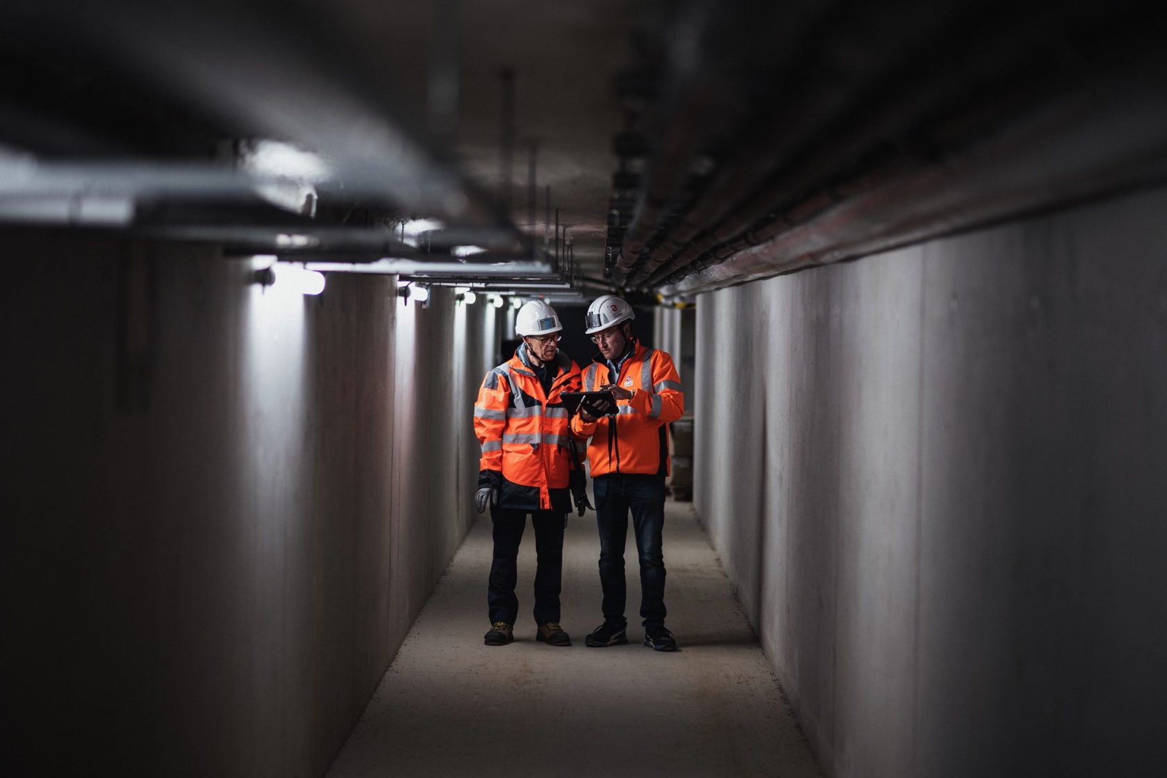 Deux techniciens en veste haute visibilité et casque de sécurité effectuent une inspection dans un couloir technique, illustrant les services d’électricité industrielle, maintenance et automatisme de Sylvestre Énergies.