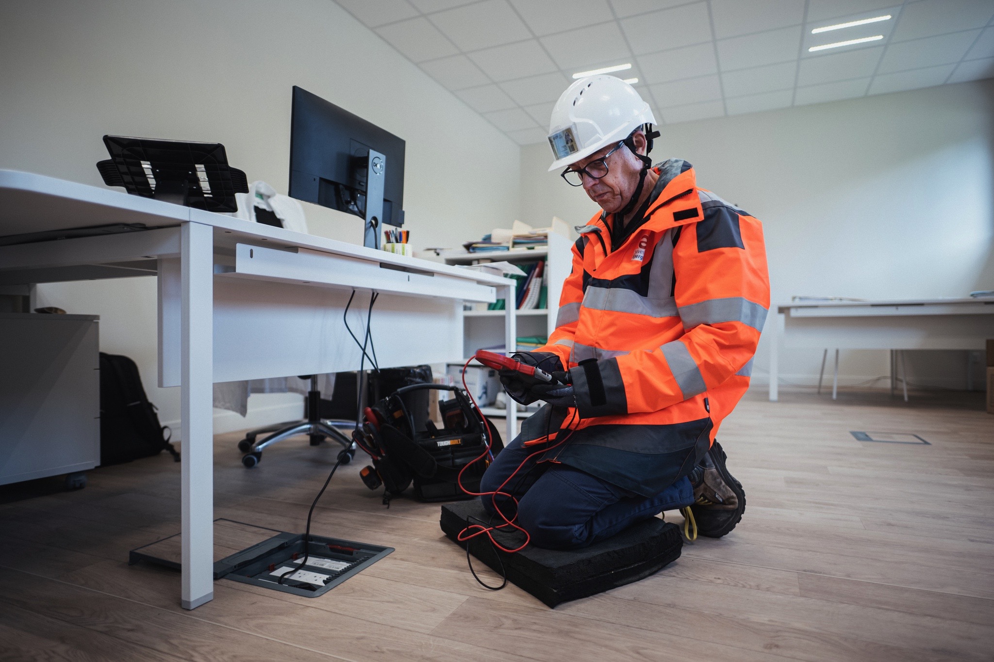 Technicien en tenue de sécurité effectuant une intervention électrique dans un bureau, illustrant les services d’électricité tertiaire, de maintenance et de sécurité proposés par Sylvestre Énergies.