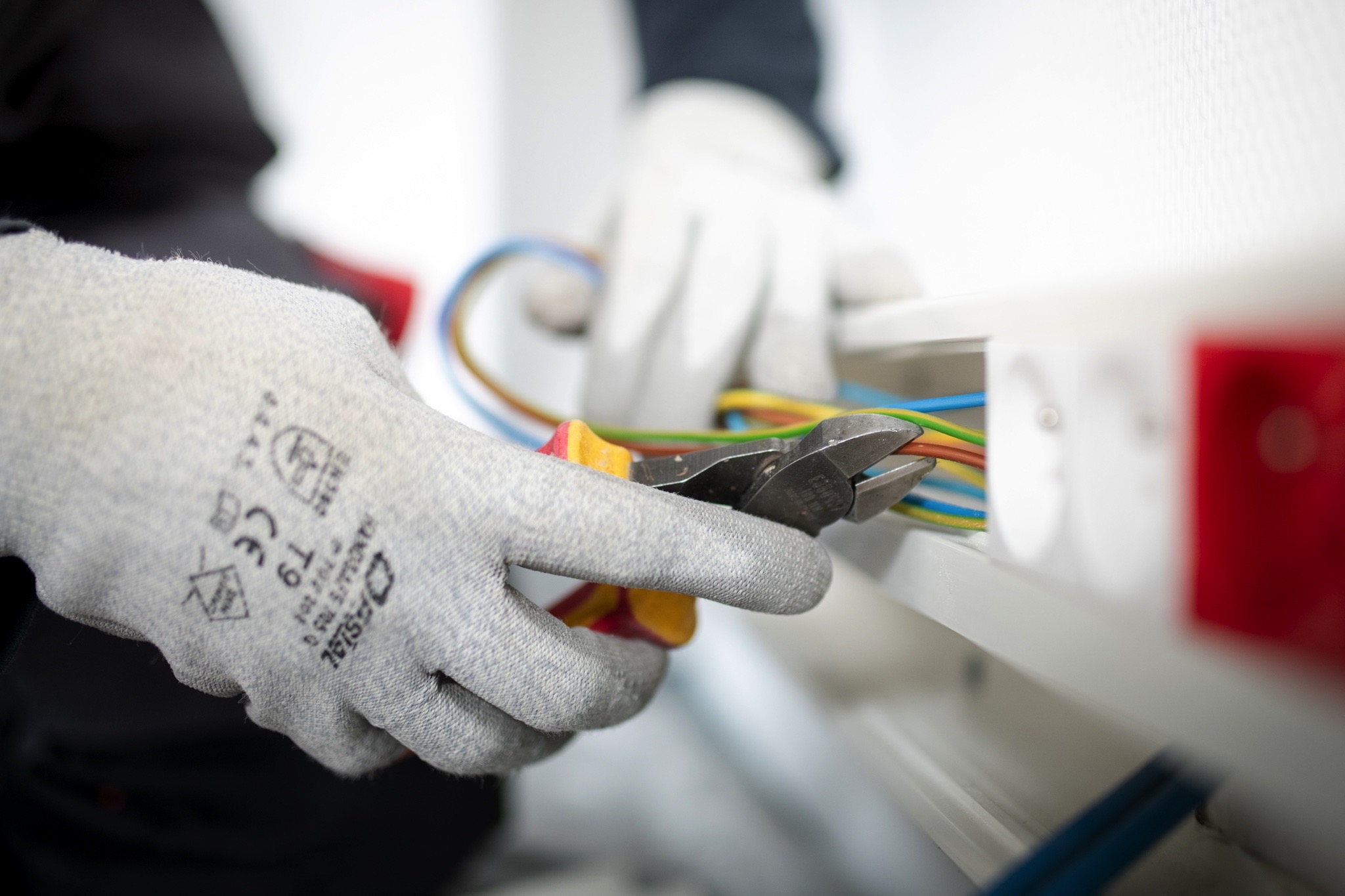 Une personne portant des gants de protection utilise une pince coupante pour couper des fils électriques multicolores.