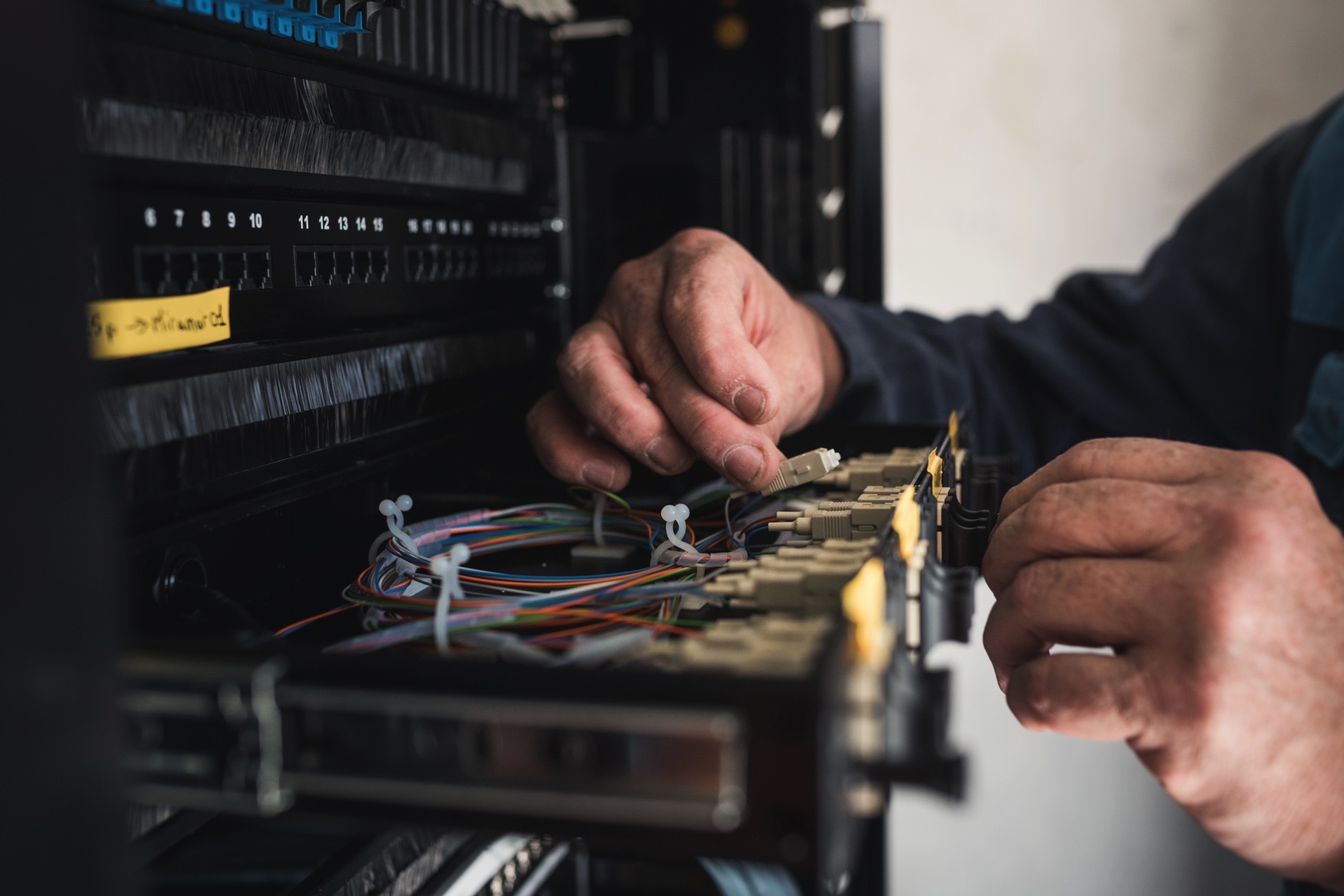 Technicien effectuant le raccordement et la maintenance de fibres optiques dans une baie informatique.