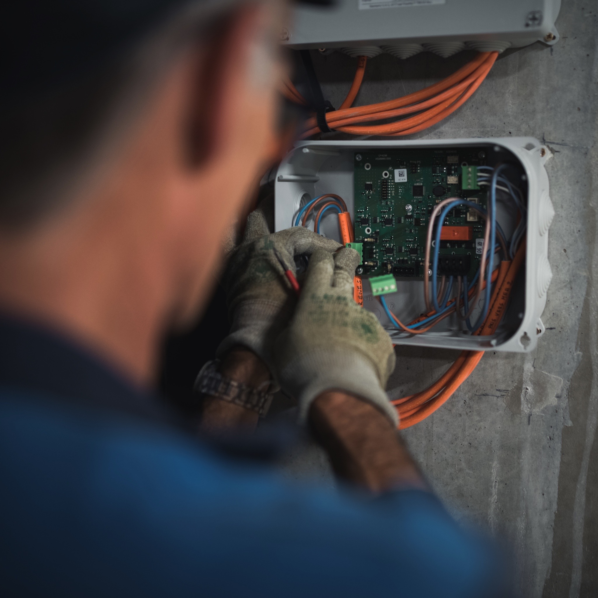 Technicien en train de câbler un boîtier électronique de courant faible avec des fils orange et une carte électronique.