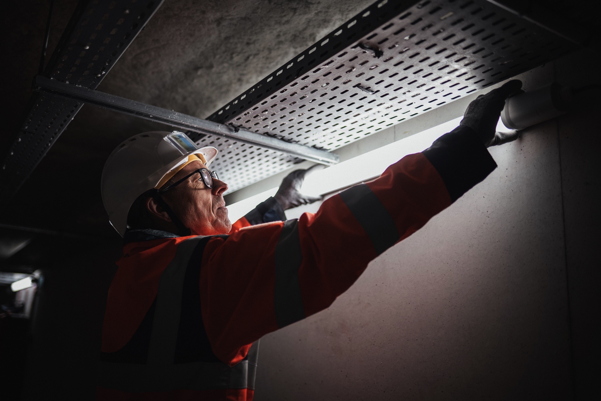 echnicien en veste haute visibilité et casque de sécurité installant un luminaire au plafond, illustrant les services d’éclairage LED, d’électricité tertiaire et de maintenance de Sylvestre Énergies.