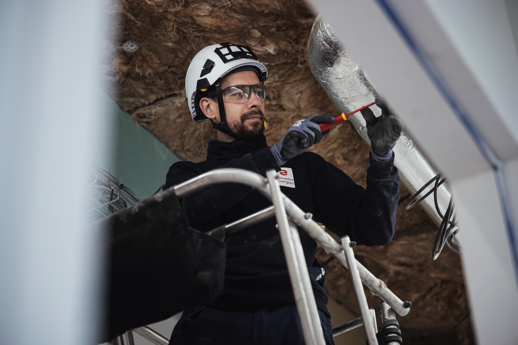Technicien réalisant le raccordement de câbles électriques sur une installation technique dans un bâtiment tertiaire.