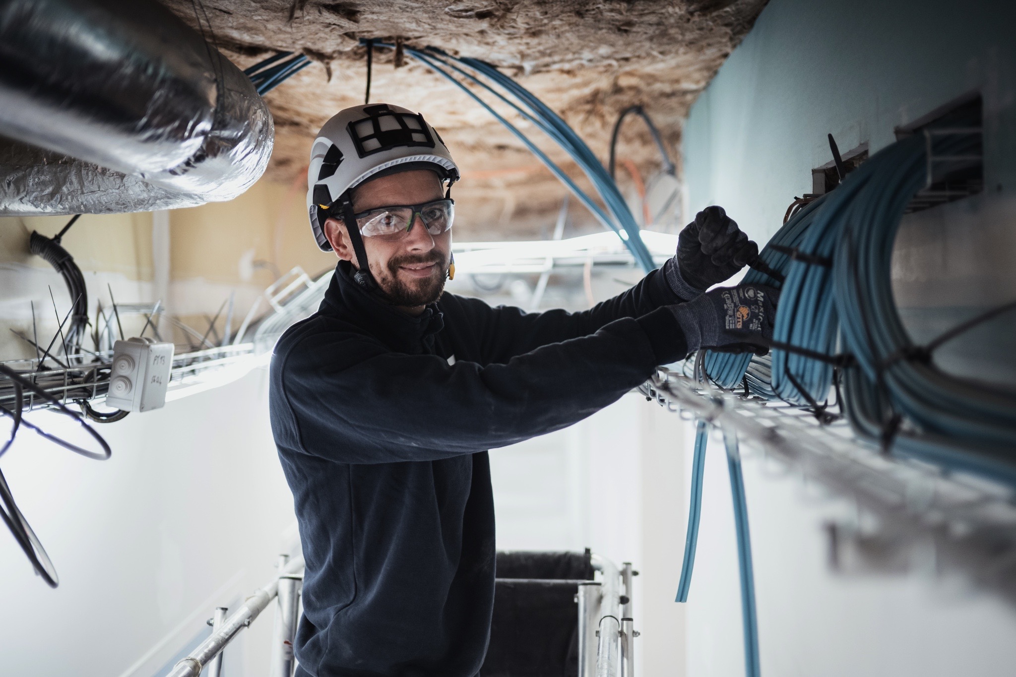 Technicien réalisant l’installation et l’organisation de câbles réseau sur un chemin de câbles dans un bâtiment tertiaire.