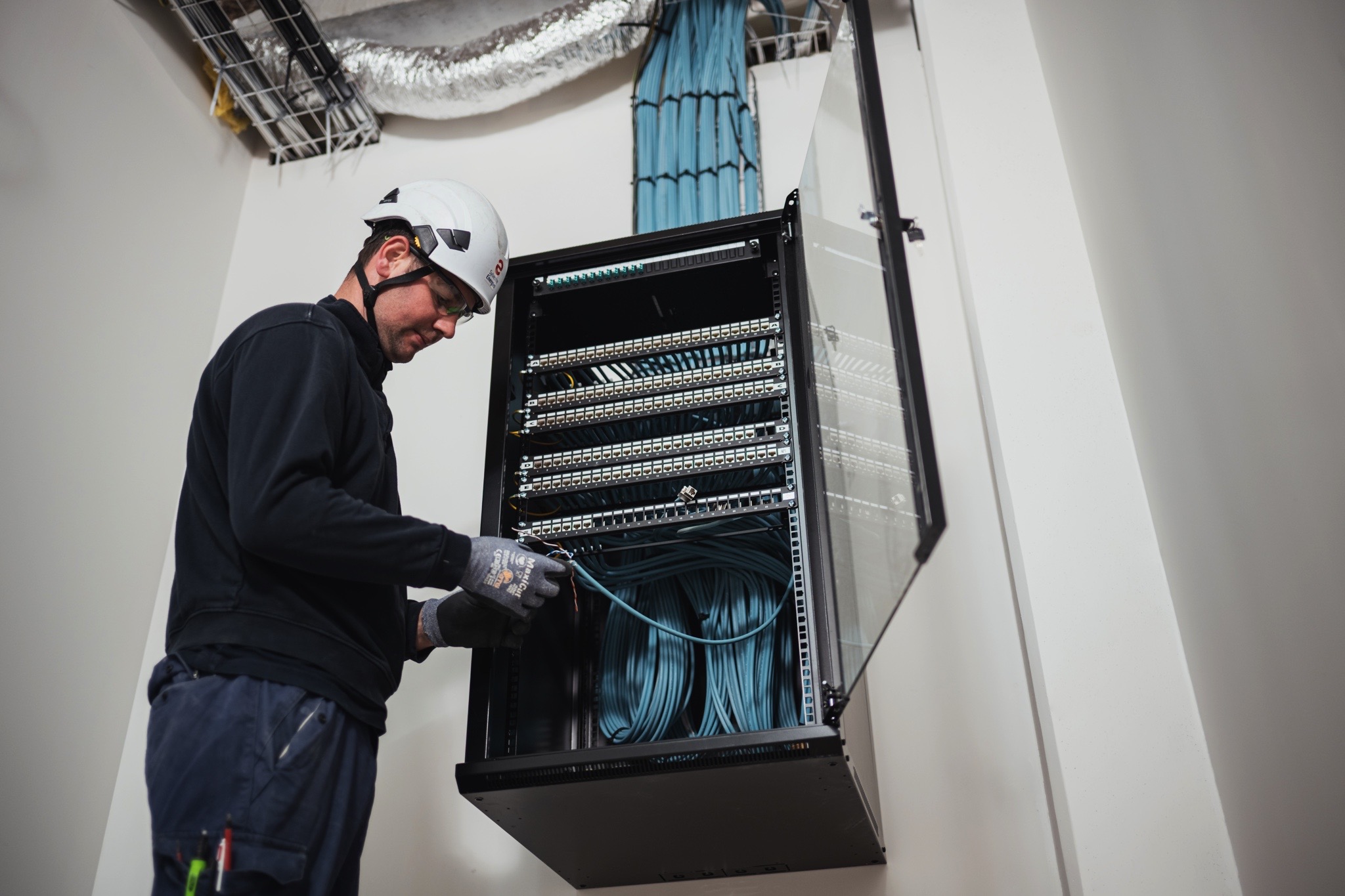 Technicien réalisant le raccordement et l’organisation des câbles dans une baie de brassage pour une infrastructure réseau et informatique.
