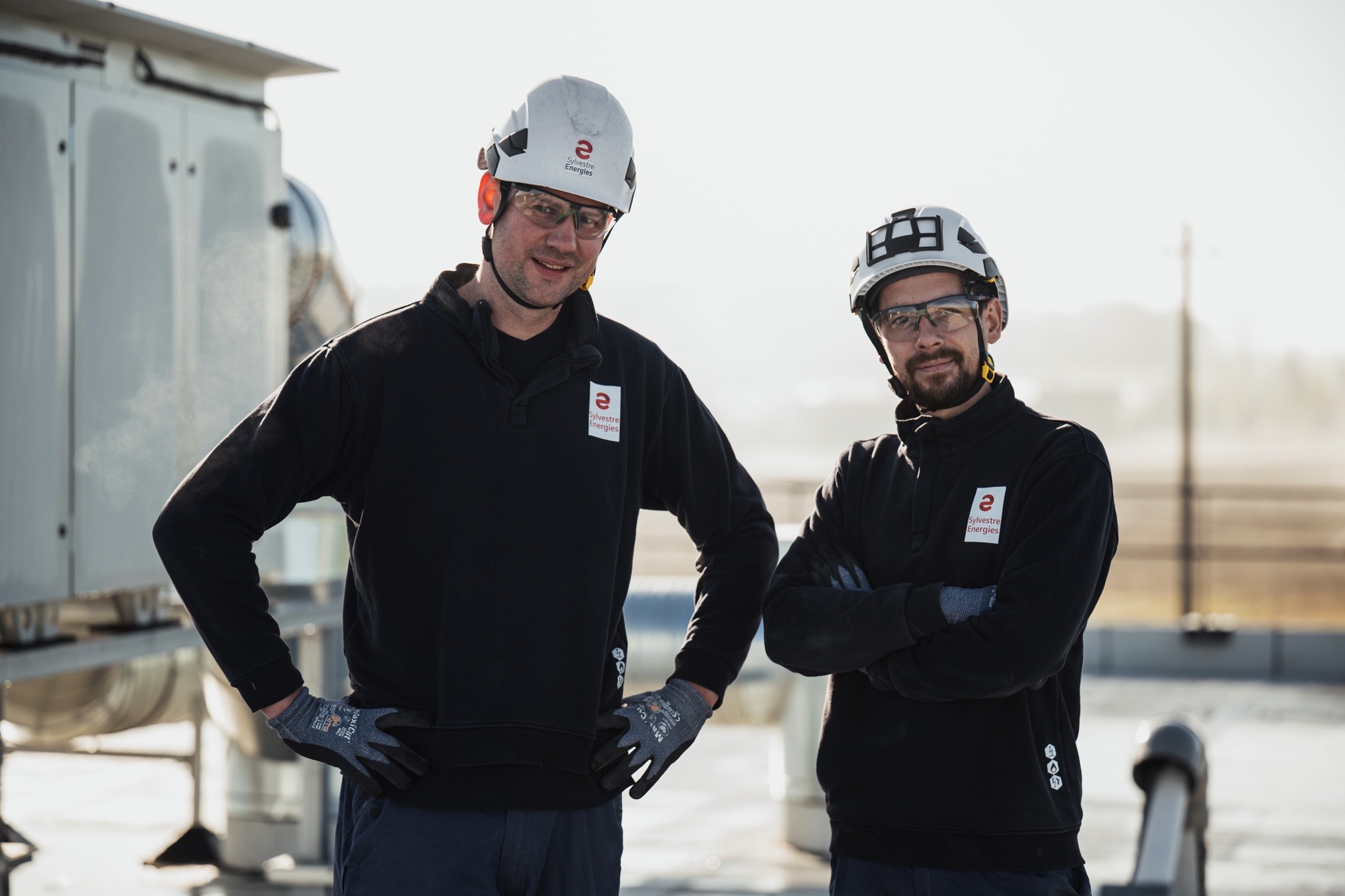 Deux techniciens équipés d’EPI sur une installation technique en toiture dans le cadre de travaux électriques et de maintenance.
