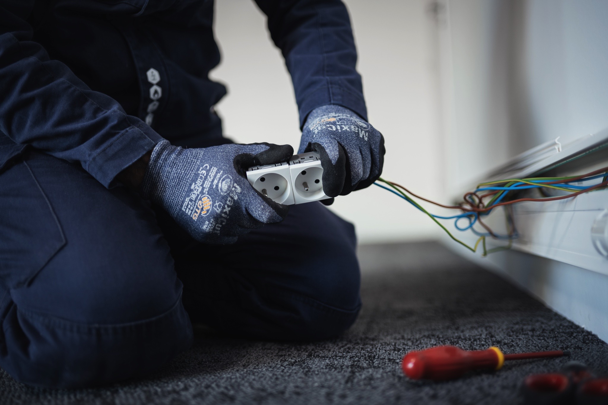 Électricien réalisant le câblage et le raccordement de prises électriques lors d’une installation électrique intérieure.