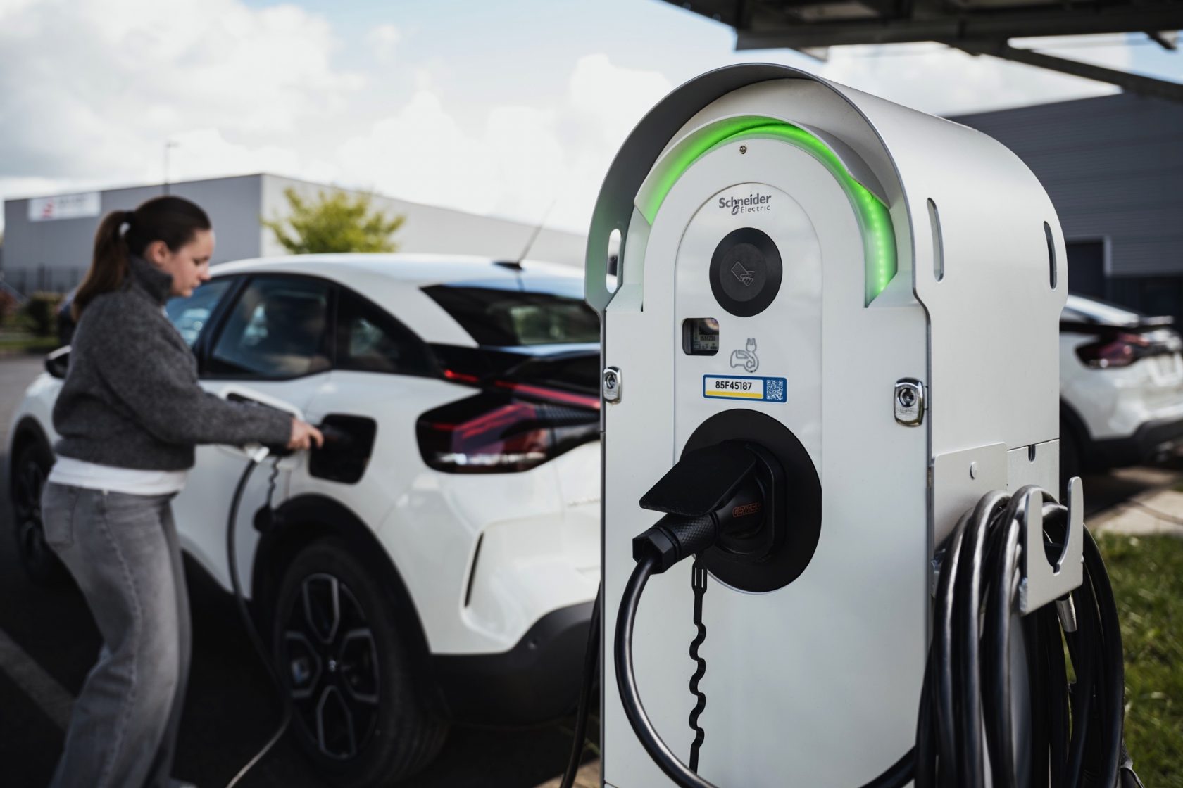 Borne de recharge pour véhicule électrique en fonctionnement sur un parking d’entreprise avec véhicule en cours de recharge.