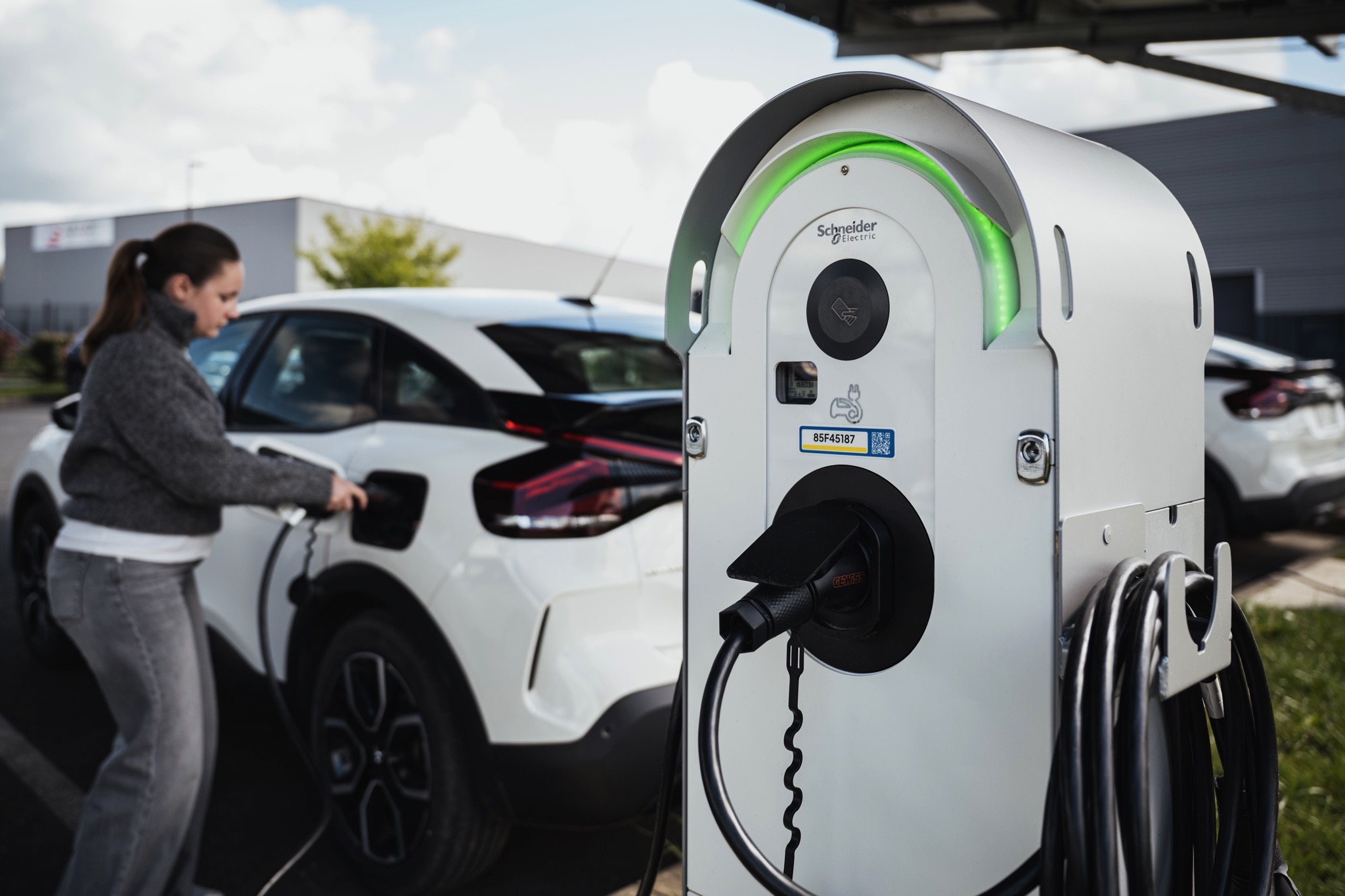 Borne de recharge pour véhicule électrique en fonctionnement sur un parking d’entreprise avec véhicule en cours de recharge.